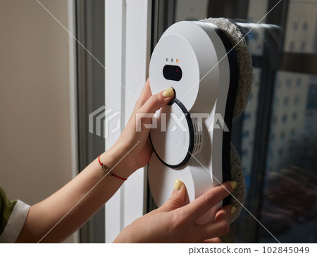 A window cleaner robot washes glass against the backdrop of multi-storey buildings. 102845049
