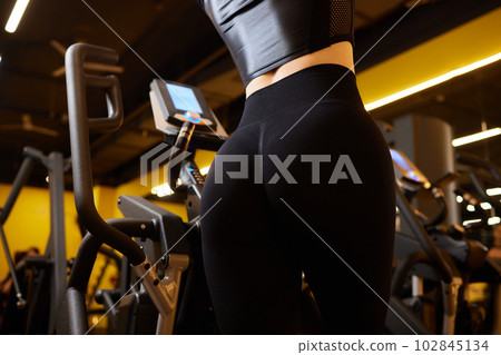 Close up portrait fit strong brunette woman in sportswear top and shorts on training ellipsoid at the gym, cardio workout. Close up portrait fit strong brunette woman in sportswear top and shorts on training ellipsoid at the gym, cardio workout. 102845134