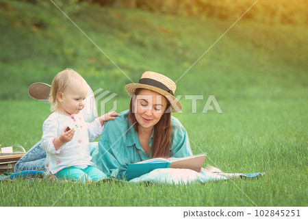 Mother is reading book for baby girl lying on the grass in the park Mother is reading book for baby girl lying on the grass in the park 102845251