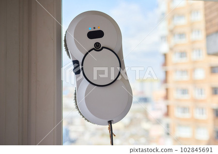A window cleaner robot washes glass against the backdrop of multi-storey buildings. 102845691