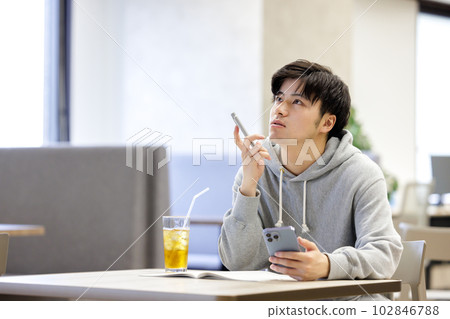 一名學生在咖啡館裡邊看智能手機邊學習 一名學生在咖啡館裡邊看智能手機邊學習 102846788