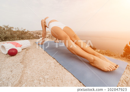 Woman sea pilates. Sporty, middle-aged woman practicing pilates in park near the sea. trains on a yoga mat and exudes a happy and active demeanor. healthy lifestyle through exercise and meditation. Woman sea pilates. Sporty, middle-aged woman practicing pilates in park near the sea. trains on a yoga mat and exudes a happy and active demeanor. healthy lifestyle through exercise and meditation. 102847923