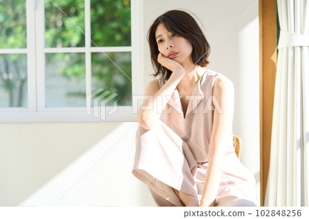 Young woman basking in the sun by the window Young woman basking in the sun by the window 102848256