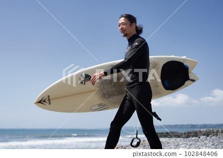 走在海灘的潛水服的中間男性衝浪者 102848406