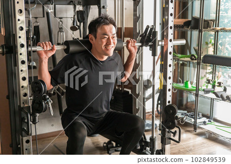 Asian man doing barbell squats in gym Asian man doing barbell squats in gym 102849539