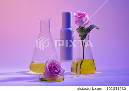 Unlabeled cosmetic container placed on a podium, glass petri dish and erlenmeyer flask of yellow fluid displayed around. Natural beauty product concept 102851380