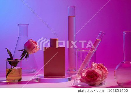 Pink perfume bottle standing on round transparent podium, displayed with laboratory glassware. Rose (Rosa) essential oil is very useful for perfume production 102851400