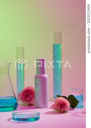Blank label bottle decorated with laboratory glassware of blue liquid and Roses. Mockup bottle for skin care cosmetic extracted from Rose (Rosa) 102851404