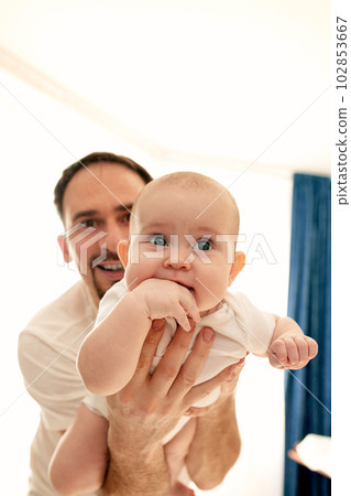 Close-up of a young happy dad holding his baby in his arms. The father hugs the child. Baby is happy in his father's arms. Close-up of a young happy dad holding his baby in his arms. The father hugs the child. Baby is happy in his father's arms. 102853667