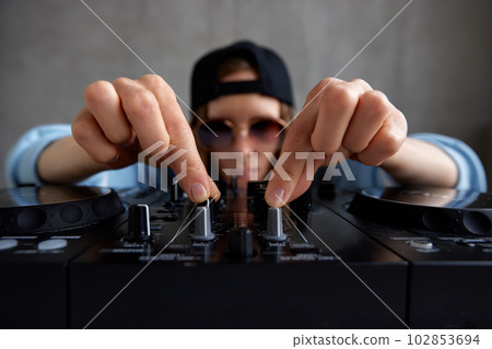 A young pretty long-haired DJ girl in a blue sweater and a black baseball cap is mixing tracks using a DJ console. Music, fun and creativity. 102853694