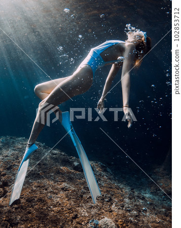 Woman freediver glides underwater in blue sea. Freediving with girl in deep ocean and sun rays Woman freediver glides underwater in blue sea. Freediving with girl in deep ocean and sun rays 102853712