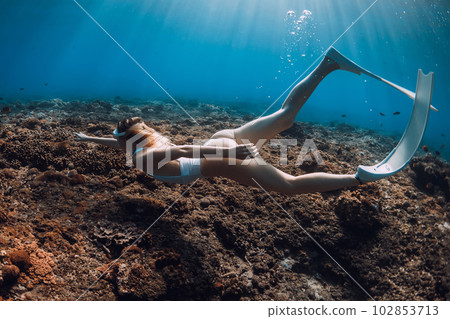 Woman freediver glide with fins underwater over corals. Freediving in tropical blue ocean Woman freediver glide with fins underwater over corals. Freediving in tropical blue ocean 102853713