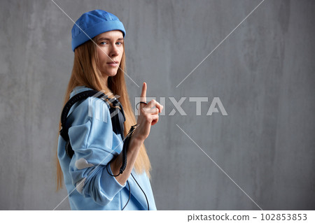 Half-length portrait of a young pretty long-haired girl in a blue sweater and cap with DJ headphones on her shoulder. Music, fun and beauty. Copy space. 102853853