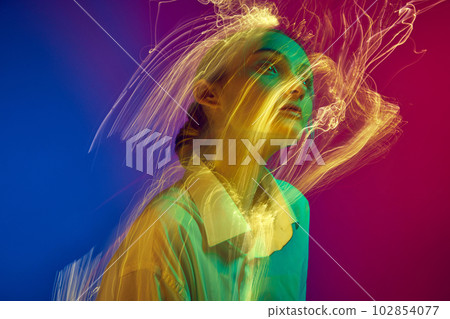 Portrait of young girl posing over gradient blue pink studio background with neon lights effect. Creative vision 102854077