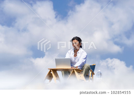 A man working on a PC under a blue sky and white clouds Workation cloud computing image A man working on a PC under a blue sky and white clouds Workation cloud computing image 102854555