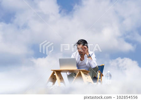 A man working on a PC under a blue sky and white clouds Workation cloud computing image 102854556