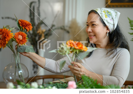 Beautiful senior woman arranging flowers in vase at her floral shop. Floristry, small business and people concept 102854835
