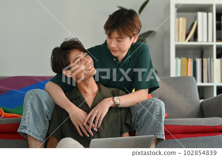 Romantic happy gay couple embracing and using laptop in living room. LGBT, love and lifestyle relationship concept 102854839