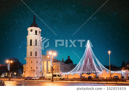 Vilnius, Lithuania. Amazing Bold Bright Blue Starry Sky Gradient Above Christmas Tree On Background Bell Tower Belfry Of Vilnius Cathedral At Square In Evening New Year Christmas Xmas Illuminations 102855919