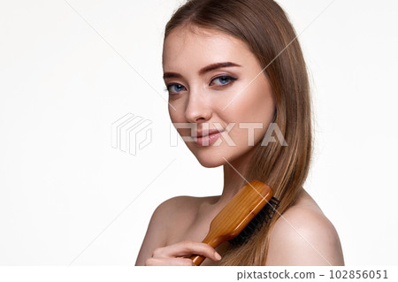 woman looks at the camera and combs her hair with wooden brush woman looks at the camera and combs her hair with wooden brush 102856051