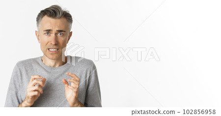 Close-up of anxious middle-aged man, looking scared and nervous, feeling guilty, standing over white background 102856958