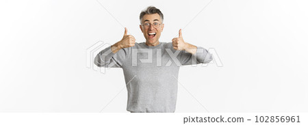 Portrait of handsome middle-aged man in glasses and grey sweater, looking excited and smiling, showing thumbs-up to approve and agree with something, like idea, standing over white background Portrait of handsome middle-aged man in glasses and grey sweater, looking excited and smiling, showing thumbs-up to approve and agree with something, like idea, standing over white background 102856961