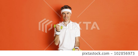 Image of handsome middle-aged male athlete, workout with dumbbells and smiling, training against orange background Image of handsome middle-aged male athlete, workout with dumbbells and smiling, training against orange background 102856973