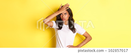 Portrait of annoyed african-american girl, slap forehead and roll her eyes bothered, forgot something important, standing over yellow background Portrait of annoyed african-american girl, slap forehead and roll her eyes bothered, forgot something important, standing over yellow background 102857017