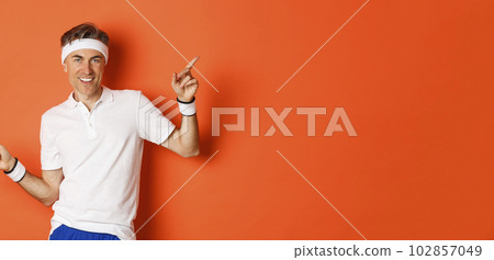 Concept of workout, sports and lifestyle. Portrait of active and healthy middle-aged guy in sportswear, smiling pleased, pointing fingers sideways and showing advertisements Concept of workout, sports and lifestyle. Portrait of active and healthy middle-aged guy in sportswear, smiling pleased, pointing fingers sideways and showing advertisements 102857049