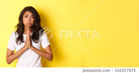 Portrait of sad african-american girl pleading, begging for help and sulking upset, standing over yellow background Portrait of sad african-american girl pleading, begging for help and sulking upset, standing over yellow background 102857073