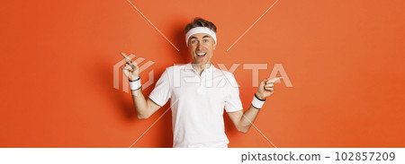 Concept of sport, fitness and lifestyle. Cheerful middle-aged sportsman with headband, smiling happy and pointing fingers sideways, showing left and right copy space 102857209