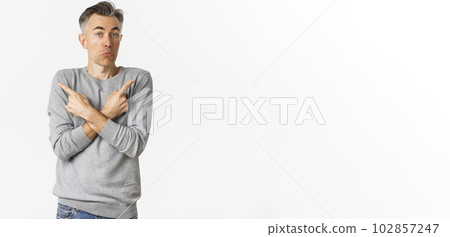 Image of handsome middle-aged man shrugging clueless, pointing fingers sideways at left and right variants, need help with choice, standing over white background 102857247