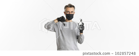 Concept of coronavirus, lifestyle and quarantine. Portrait of middle-aged man in medical mask and gloves do not recommend antiseptic, showing hand sanitizer and thumbs-down, white background 102857248
