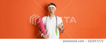 Concept of workout, gym and lifestyle. Close-up of happy and satisfied middle-aged athlete, showing thumb-up, like training session, holding yoga mat and skipping rope for fitness 102857272