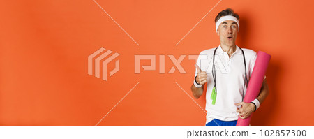 Concept of workout, gym and lifestyle. Close-up of happy and satisfied middle-aged athlete, showing thumb-up, like training session, holding yoga mat and skipping rope for fitness 102857300