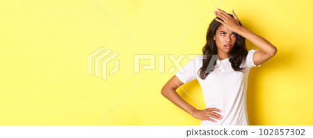 Portrait of annoyed african-american girl, slap forehead and roll her eyes bothered, forgot something important, standing over yellow background Portrait of annoyed african-american girl, slap forehead and roll her eyes bothered, forgot something important, standing over yellow background 102857302