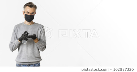 Concept of coronavirus, lifestyle and quarantine. Image of middle-aged man in medical mask and gloves, applying hand sanitizer, preventing catching covid-19, white background 102857320