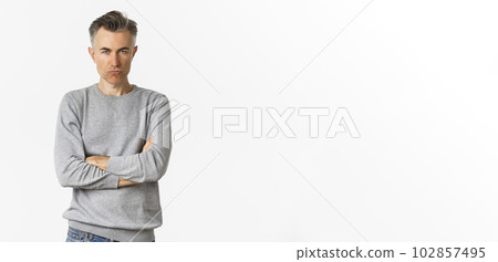 Image of angry middle-aged man feeling offended, cross arms on chest and squinting at camera, standing over white background Image of angry middle-aged man feeling offended, cross arms on chest and squinting at camera, standing over white background 102857495