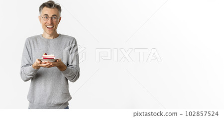 Portrait of happy handsome middle-aged man, wearing glasses and gray sweater, holding cake and looking amazed at camera, standing over white background Portrait of happy handsome middle-aged man, wearing glasses and gray sweater, holding cake and looking amazed at camera, standing over white background 102857524