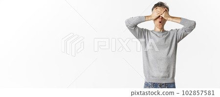 Image of excited middle-aged guy in grey sweater, cover eyes with hands and looking amazed while waiting for surprise, playing hide-n-seek, standing over white background Image of excited middle-aged guy in grey sweater, cover eyes with hands and looking amazed while waiting for surprise, playing hide-n-seek, standing over white background 102857581