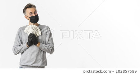 Concept of covid-19, social distancing and lifestyle. Portrait of cheerful rich man in medical mask, gloves and glasses, bragging with money and looking pleased, winning lottery 102857589