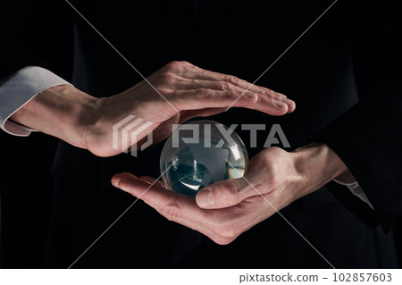businessman's hands are covered with a glass ball on a black background businessman's hands are covered with a glass ball on a black background 102857603