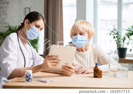 Female doctor and senior woman, patient wearing face mask, having appointment in office. Checkup and treatment after virus 102857715