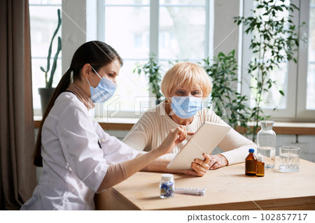 Female doctor and senior woman, patient wearing face mask, having appointment in office. Checkup and treatment after virus 102857717