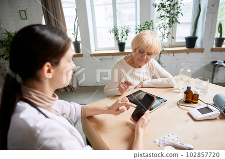 Senior woman and female doctor using gadgets to check patient's health information. In office. Modern medical attitude Senior woman and female doctor using gadgets to check patient's health information. In office. Modern medical attitude 102857720
