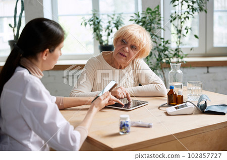 Senior woman visiting doctor, therapist for check up, asking questions about her treatment. Doctor checking information about patient's health Senior woman visiting doctor, therapist for check up, asking questions about her treatment. Doctor checking information about patient's health 102857727