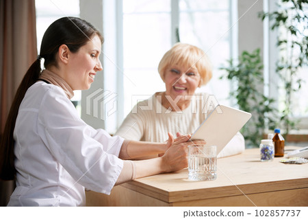 Senior woman visiting doctor, sitting at table in office, having appointment and consultation. Good result after treatment 102857737