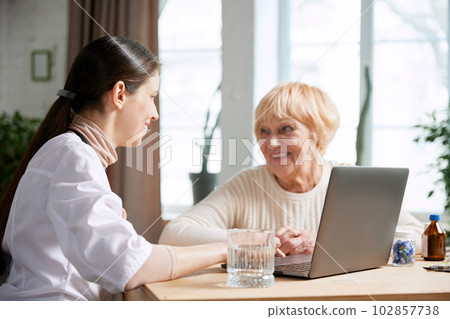 Senior woman visiting doctor, sitting at table in office, having appointment and consultation. Women smiling and talking 102857738