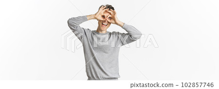 Portrait of funny middle-aged guy making faces, showing hand glasses around eyes as if looking through binoculars, standing over white background 102857746
