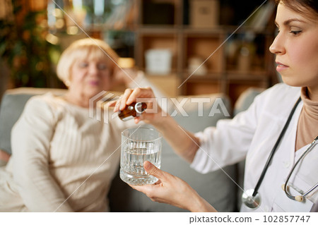 Female doctor dropping meds, drops for her senior female patient sitting on couch. Taking care after health with medicine 102857747